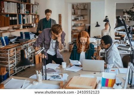 Young creative team working on project in busy design studio office Royalty-Free Stock Photo #2410552123