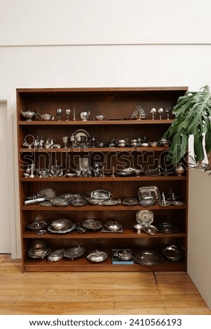 Dark timber cabinet displaying silverware in thrift store Royalty-Free Stock Photo #2410566193