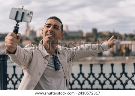 Young content creator filming himself with his cell phone on a tripod while talking to his followers. Boy filming with his cell phone pointing the river and the city of Budapest.
