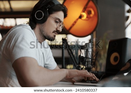 With meticulous care, an audio specialist edits music on his laptop in a studio, surrounded by professional recording equipment