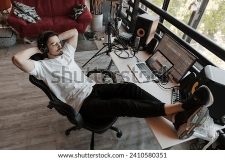 Audio specialist takes a thoughtful break, reclining in his chair amidst a studio setup with editing software on display