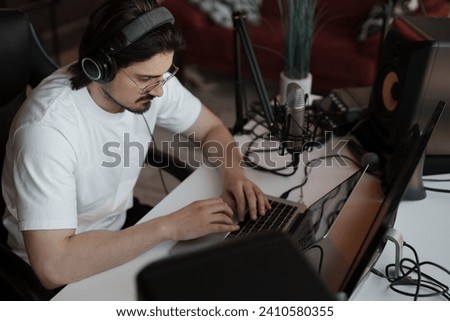An audio producer immersed in his work, editing tracks on a laptop in a professional home studio setup
