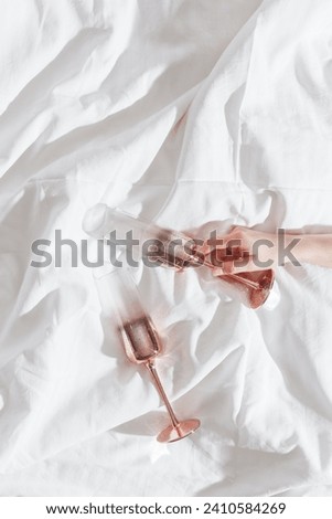 Pink color shining champagne glass in female hand on bed. Lifestyle aesthetic photo, star filter effect. Valentine's Day holiday, love concept, romance meeting. Festive Sparkling wine in wineglasses.