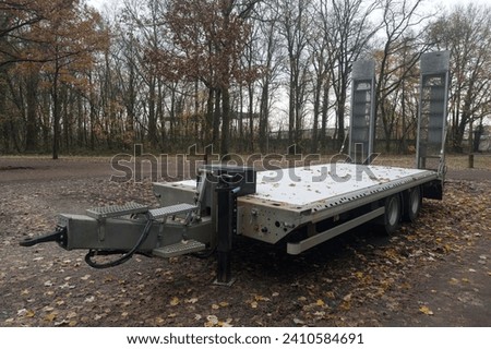 Empty car trailer for transporting construction equipment against the backdrop of an autumn landscape.