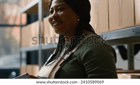 Close up shot of african american warehouse logistics director holding tablet, checking packaged cardboard boxes parcels, ensuring optimal operations in professional storage depository Royalty-Free Stock Photo #2410589069