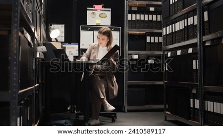 Dedicated female private detective accurately conducts research for clues and information. Using technology in office room, caucasian police officer examines evidence files and does forensic analysis. Royalty-Free Stock Photo #2410589117