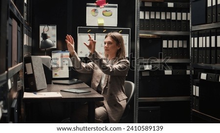 Caucasian female private investigator uses modern technology to analyze holographic clues and criminal records. Police officer using artificial intelligence to move holographic 3D picture of evidence.