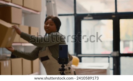 Warehouse advertising professional using smartphone to make branding video for social media. Influencer filming herself in storage room showcasing company daily tasks to attract new employees