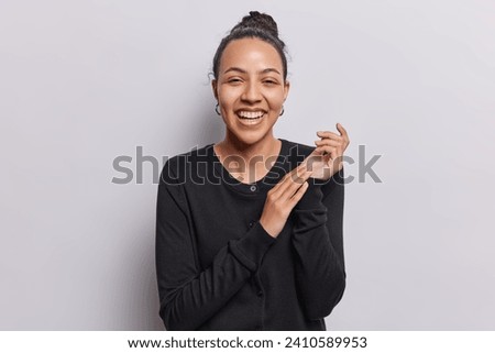 Horizontal shot of cheerful pretty Latin woman rubs palms and laughs joyfully hears funny joke from friend expresses positive sincere emotions wears black jumper isolated over white background Royalty-Free Stock Photo #2410589953