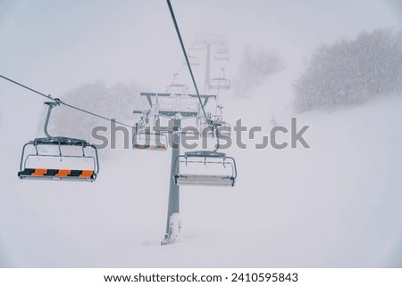 Quadruple chairlift rises above snowy forest to misty mountain Royalty-Free Stock Photo #2410595843