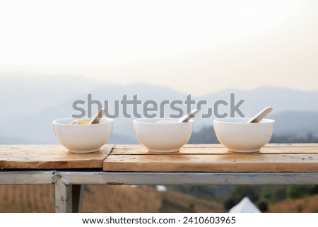 Boiled rice with boiled egg, pork, coriander, and fried garlic in white bowl. Breakfast with beautiful natural landscape.