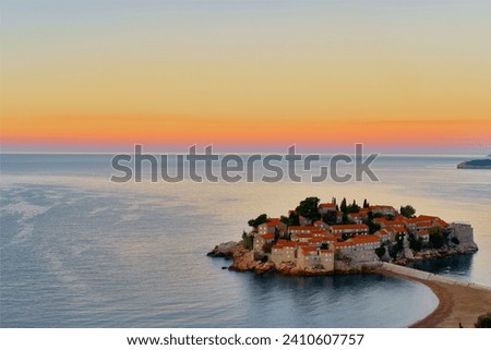 Sveti Stefan at sunset. Deserted winter beach. Colorful sky reflecting in the Adriatic sea and old stone houses. Royalty-Free Stock Photo #2410607757