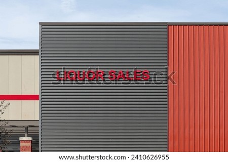 A grey exterior wall of a wholesale business with large red text letters. The liquor sales signage is displayed for the sale of beverages such as beer, wine and spirits at an alcohol retail company.