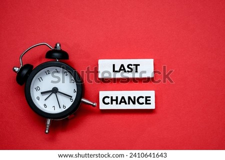 Top view of black alarm clock sitting next to a wooden block written “LAST CHANCE” on it. Copy space concept Royalty-Free Stock Photo #2410641643