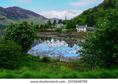 Country homes nestled in the Scottish highlands reflected in lake Royalty-Free Stock Photo #2410648785