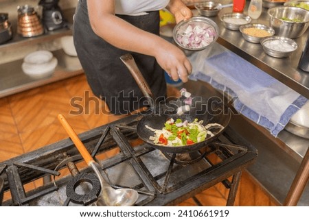 Top view of the hands of a cook frying mixed vegetables in a pan in a commercial kitchen