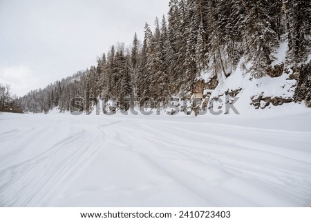 Winter road along the bed of a frozen river, cold weather, winter forest, taiga. White snow, snowdrifts on the river, mountainous terrain. High quality photo