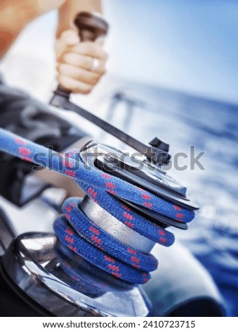 Holder of rope on sailboat, man pulling handle of spool, macro photo of yacht detail, working on water transport, luxury summer time sport Royalty-Free Stock Photo #2410723715