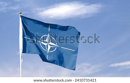 NATO flag on cloudy sky. flying in the sky Royalty-Free Stock Photo #2410731421