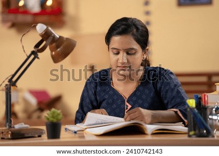 Indian teenager dedicated girl preparing for government or public examination by reading at home - concept of concentration, education and aspirant. Royalty-Free Stock Photo #2410742143