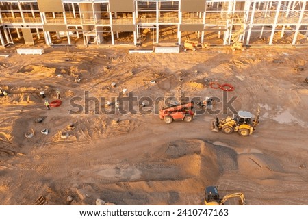 Drone photography of constructions site of large commercial building with construction machinery and construction workers during autumn sunny morning