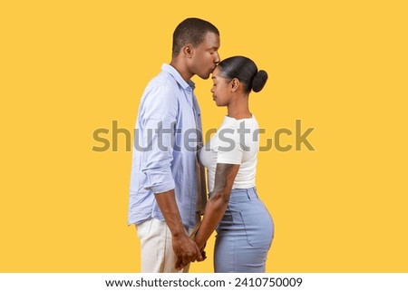 In tender display of affection, black couple stands close, foreheads touching and hands clasped, evoking sense of intimacy against yellow background Royalty-Free Stock Photo #2410750009