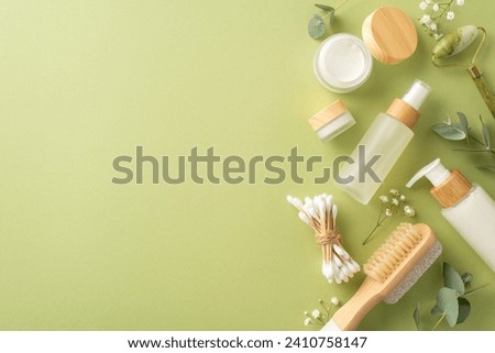 Eco-friendly self-care setup. Top view photo showcasing gua sha tool, lotion, cream bottles, cotton buds, flowers and more on a light green surface. Ideal for promoting a hygienic lifestyle
