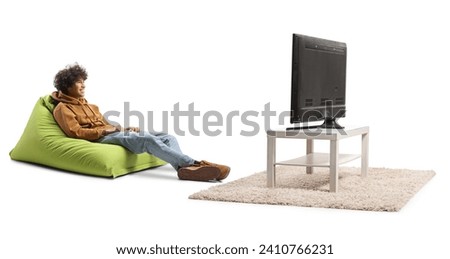 Guy sitting on a green bean bag chair and watching tv isolated on white background Royalty-Free Stock Photo #2410766231