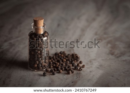 A small glass bottle filled with organic Black pepper (Piper nigrum) is placed on a marble background. Royalty-Free Stock Photo #2410767249