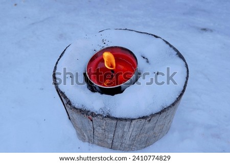 A warm candlelight on a snow-covered tree trunk in the middle of winter Royalty-Free Stock Photo #2410774829