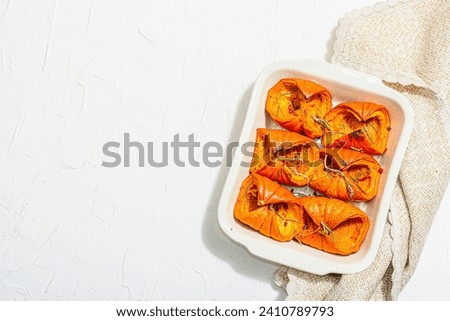 Oven baked pumpkin slices with honey, rosemary and seeds. Healthy vegan food, trendy hard light, dark shadow. White background, flat lay, top view Royalty-Free Stock Photo #2410789793