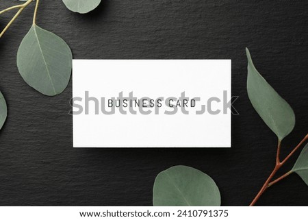 Business card and eucalyptus branches on black background, top view