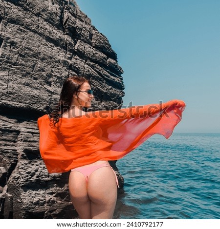 Happy tourist in bikini enjoys taking photos in nature for memories. A female traveler poses on a beach by the sea surrounded by volcanic rocks and shares the joy of travel and freedom.