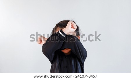Little Asian girl covers her eyes with her hand, on a gray background. The child is tired, crying and rubbing her eyes with her hands. Copy space.