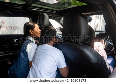 A young Indian boy and his pre-teen sister, sitting in the backseat of their car