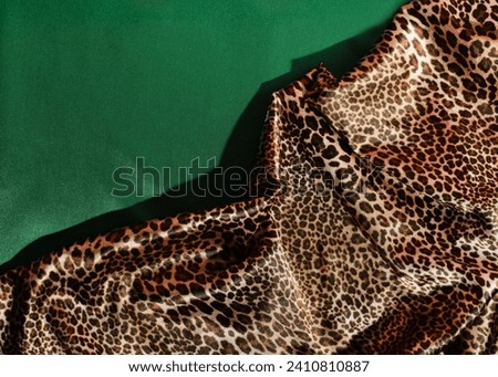 Animal print satin fabric on a deep green background, fashionable color and print combination, creative copy space.
