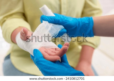 Doctor bandaging patient's burned hand indoors, closeup Royalty-Free Stock Photo #2410812701