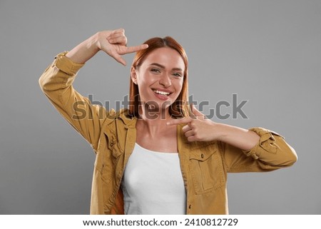 Casting call. Young woman showing frame gesture on grey background