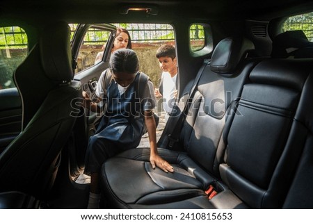 A pre-teen Indian girl and her younger brother, wearing school uniforms with backpacks, get into their car as their mother holds the door for them, on the way to drop them to school in Mumbai, India.