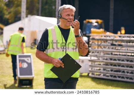 Male Production Worker With Headset Setting Up Outdoor Stage For Music Festival Or Concert Royalty-Free Stock Photo #2410816785
