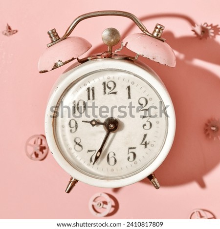 Vintage alarm clock on a pastel pink background, gears and clockwork parts in the background.