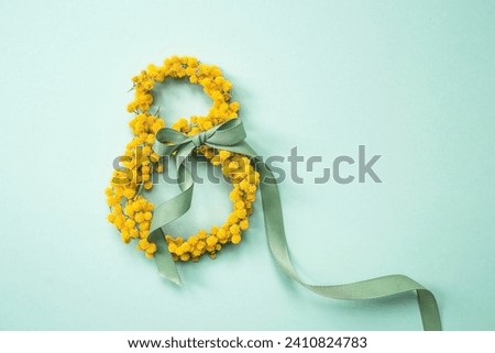 International Women's Day. A banner, a flyer, a beautiful postcard for March 8th. Yellow mimosa flowers in the shape of the number eight and a ribbon bow on a turquoise, blue background. Royalty-Free Stock Photo #2410824783