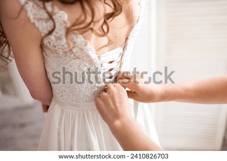 A caring Fairy Godmother lovingly assists the bride as she perfects her wedding dress before the magical ceremony. Royalty-Free Stock Photo #2410826703