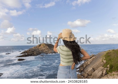 woman from behind holding her hat in the breeze with the maritime background
