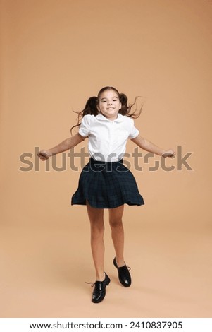 Cute schoolgirl jumping on beige background, space for text Royalty-Free Stock Photo #2410837905