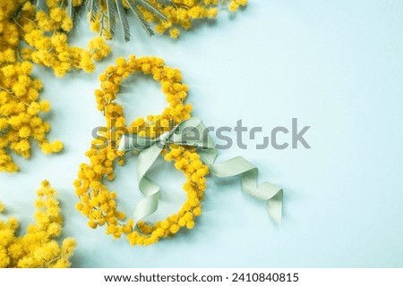 International Women's Day. A banner, a flyer, a beautiful postcard for March 8th. Yellow mimosa flowers in the shape of the number eight and a ribbon bow on a turquoise, blue background. Royalty-Free Stock Photo #2410840815