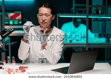 Young asian researcher attentively examining particle of raw meat while working in laboratory