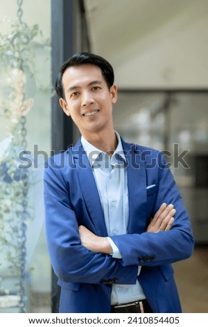 Confident young Asian businessman sitting with arms crossed smiling looking at camera in the office.