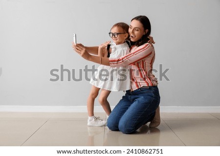 Beautiful mother and her cute little daughter with mobile phone taking selfie near grey wall