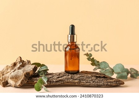 Bottle of cosmetic oil with eucalyptus branches and tree bark on pale yellow background Royalty-Free Stock Photo #2410870323